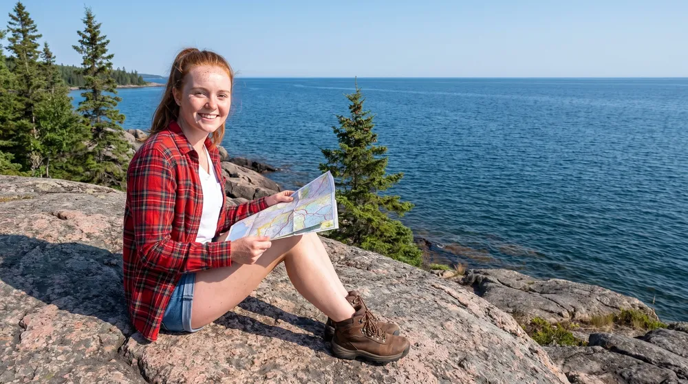 Ellie Marchand sits on pink-grey granite on the shore of Lake Superior with a folded road map on her lap.